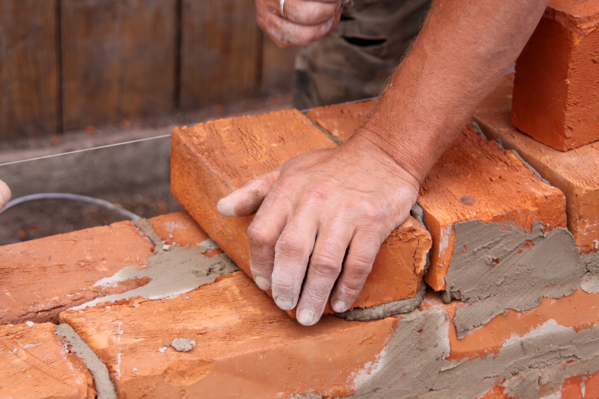 Mason hands building brick wall